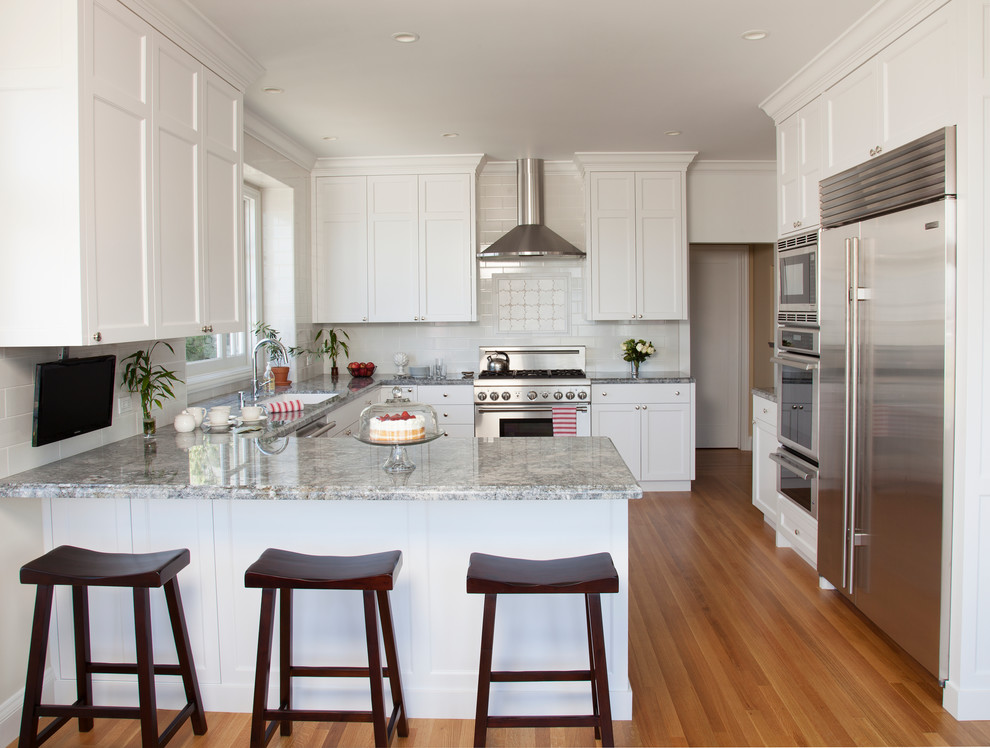 Inspiration for a large traditional u-shaped separate kitchen in San Francisco with an undermount sink, shaker cabinets, white cabinets, granite benchtops, white splashback, ceramic splashback, stainless steel appliances, medium hardwood floors and a peninsula.