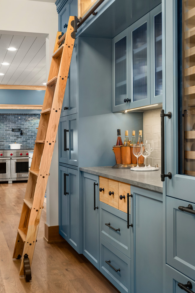 Inspiration for a small beach style galley home bar in Minneapolis with no sink, recessed-panel cabinets, blue cabinets, quartzite benchtops, grey splashback, ceramic splashback, medium hardwood floors, brown floor and grey benchtop.