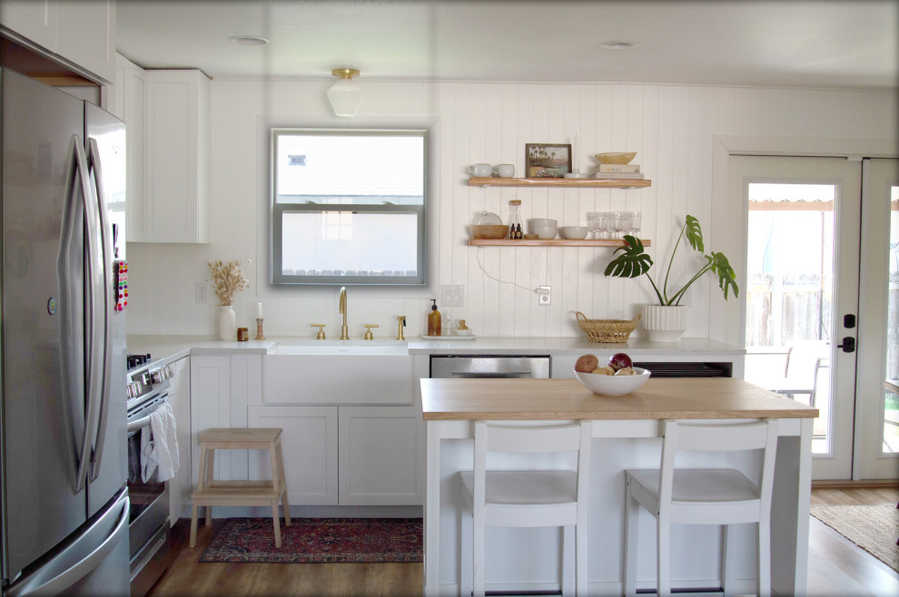 Photo of a mid-sized scandinavian eat-in kitchen in Los Angeles with a farmhouse sink, shaker cabinets, white cabinets, shiplap splashback, stainless steel appliances, medium hardwood floors and with island.