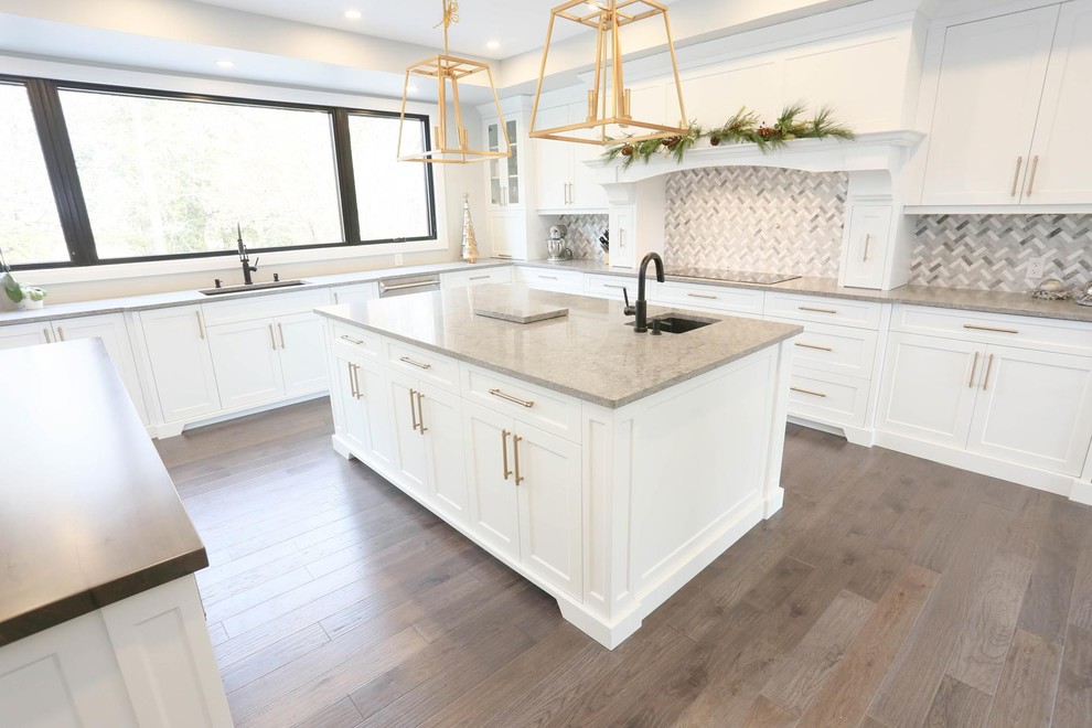Example of a large transitional u-shaped dark wood floor and brown floor enclosed kitchen design with an undermount sink, shaker cabinets, white cabinets, granite countertops, gray backsplash, mosaic tile backsplash, stainless steel appliances, two islands and gray countertops