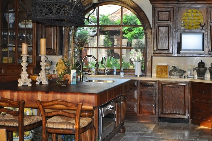 This is an example of an expansive mediterranean u-shaped open plan kitchen in Houston with an integrated sink, recessed-panel cabinets, dark wood cabinets, limestone benchtops, beige splashback, stone slab splashback, stainless steel appliances, travertine floors and with island.