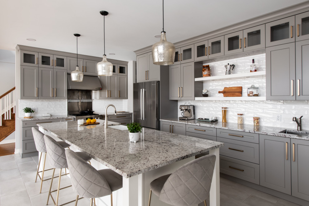 Example of a mid-sized transitional l-shaped porcelain tile and gray floor open concept kitchen design in Ottawa with a farmhouse sink, shaker cabinets, gray cabinets, granite countertops, white backsplash, ceramic backsplash, stainless steel appliances, an island and multicolored countertops