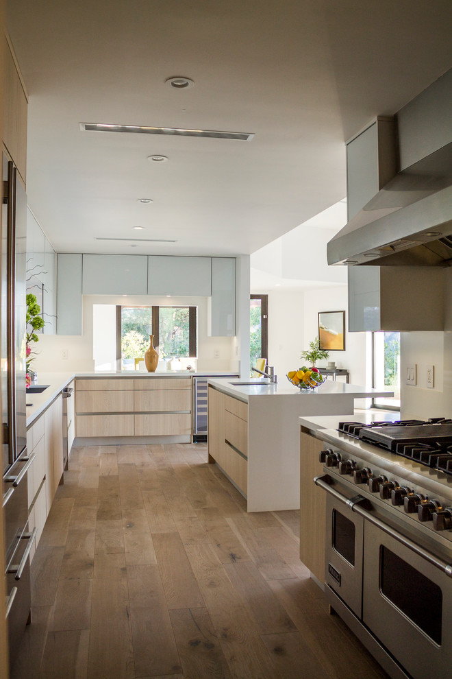 Inspiration for a large midcentury l-shaped open plan kitchen in Los Angeles with an integrated sink, flat-panel cabinets, light wood cabinets, laminate benchtops, stainless steel appliances, medium hardwood floors and with island.