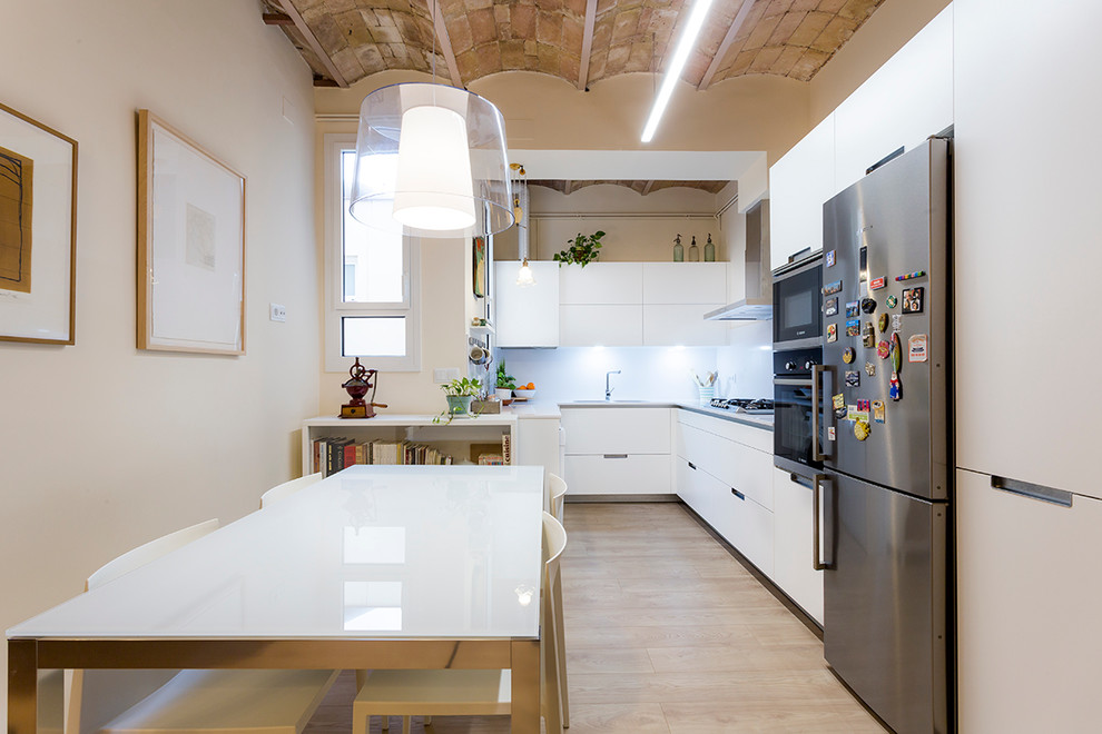 Mid-sized industrial l-shaped open plan kitchen in Barcelona with quartz benchtops, flat-panel cabinets, white cabinets and no island.