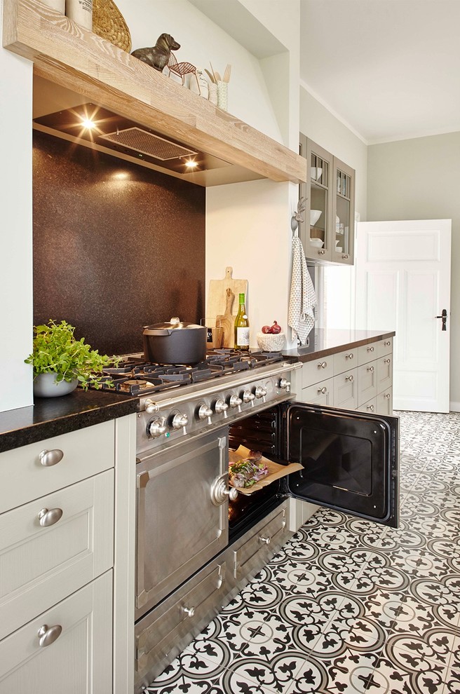 Design ideas for an expansive traditional galley separate kitchen in Berlin with an undermount sink, beaded inset cabinets, grey cabinets, granite benchtops, black splashback, stone tile splashback, black appliances, porcelain floors and with island.