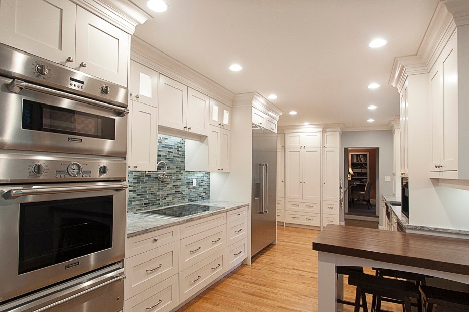 Example of a transitional medium tone wood floor kitchen design with shaker cabinets, white cabinets, granite countertops, brown backsplash, matchstick tile backsplash and stainless steel appliances