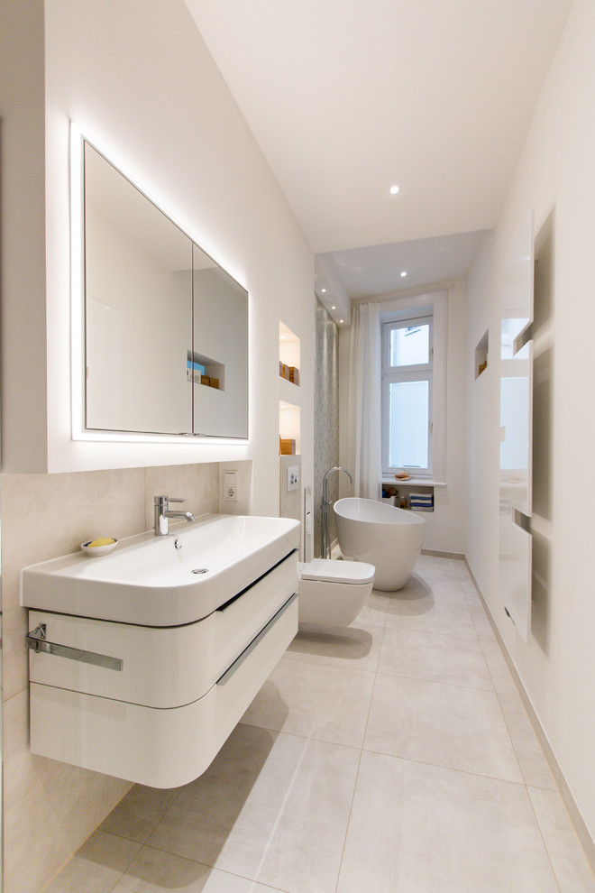 This is an example of a mid-sized contemporary 3/4 bathroom in Hamburg with flat-panel cabinets, white cabinets, a freestanding tub, a curbless shower, a wall-mount toilet, white walls, an integrated sink, a hinged shower door, beige tile, cement tile, cement tiles, solid surface benchtops and beige floor.