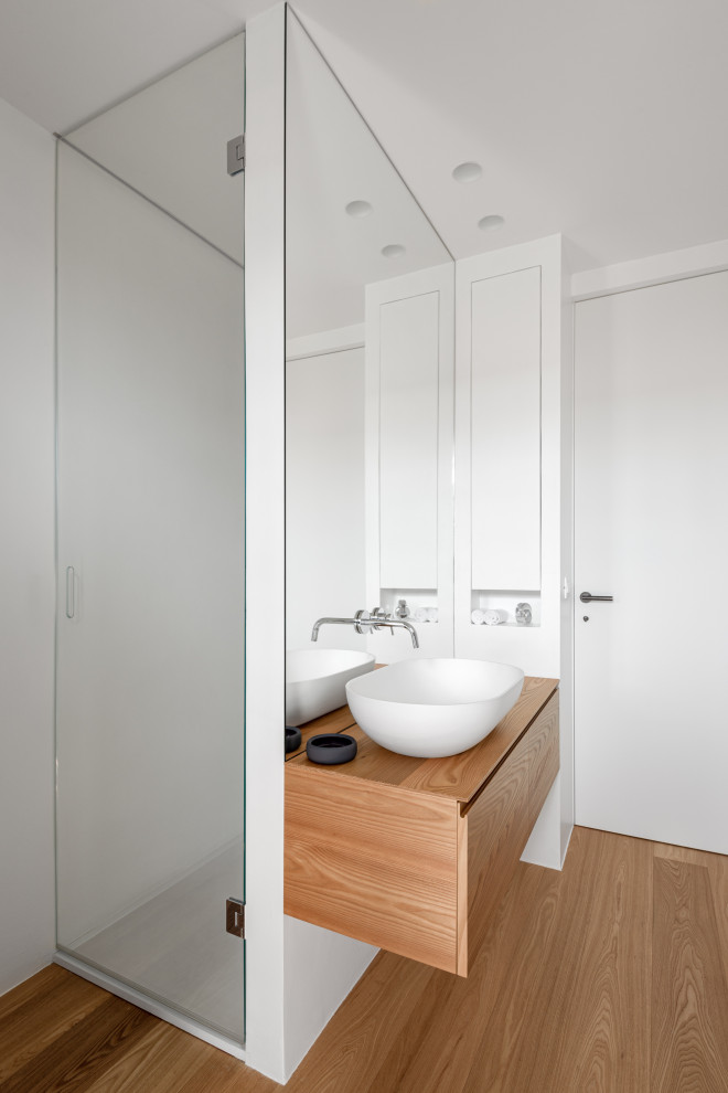 Design ideas for a mid-sized contemporary 3/4 wet room bathroom in Venice with light wood cabinets, a two-piece toilet, white tile, mirror tile, white walls, light hardwood floors, a vessel sink, solid surface benchtops, beige floor, a hinged shower door, white benchtops, a niche, a single vanity, a floating vanity and flat-panel cabinets.