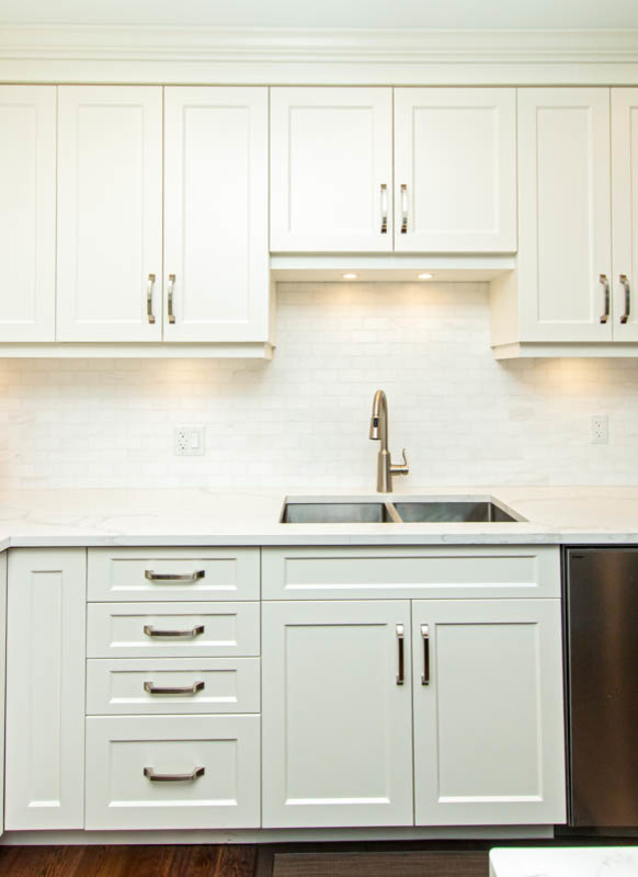 Open concept kitchen - mid-sized transitional l-shaped medium tone wood floor and brown floor open concept kitchen idea with an undermount sink, shaker cabinets, white cabinets, quartzite countertops, white backsplash, stone tile backsplash, stainless steel appliances, an island and white countertops