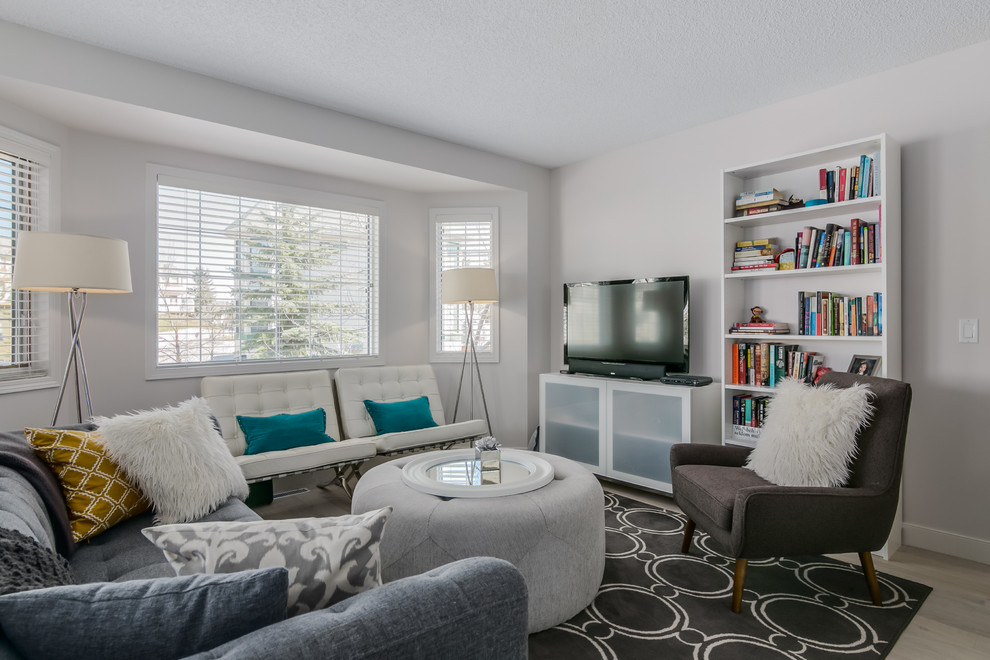 Photo of a mid-sized contemporary enclosed family room in Calgary with white walls, light hardwood floors, no fireplace and a freestanding tv.