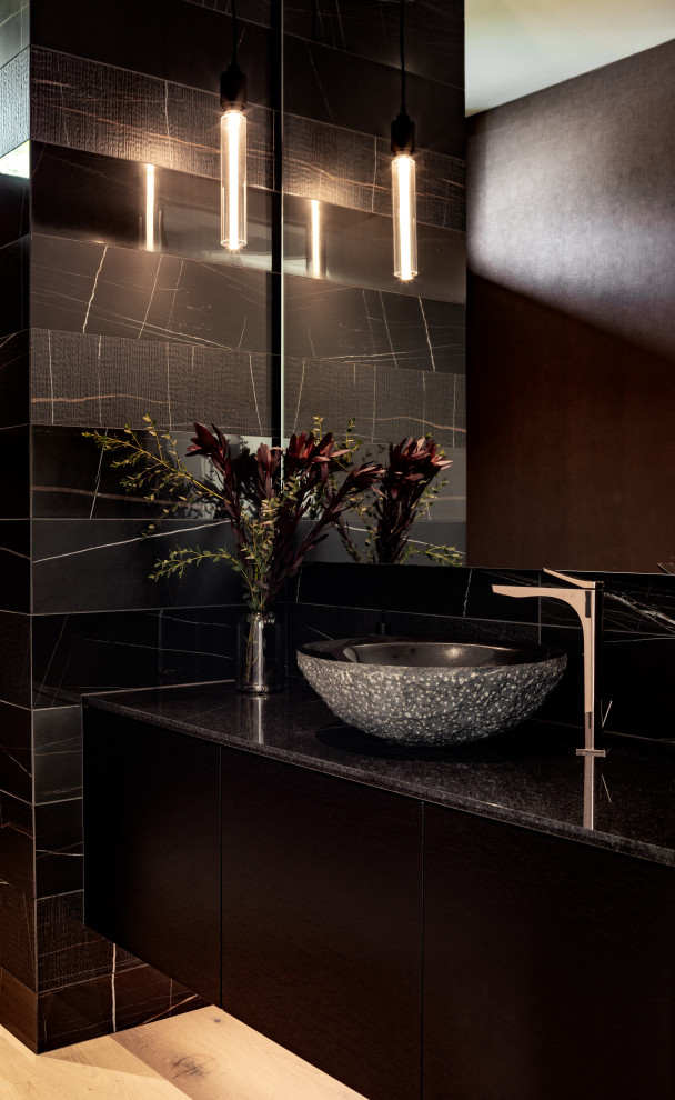 Photo of a mid-sized contemporary powder room in Vancouver with flat-panel cabinets, black cabinets, a wall-mount toilet, black tile, porcelain tile, white walls, light hardwood floors, a vessel sink, granite benchtops, beige floor, black benchtops, a floating vanity and wallpaper.