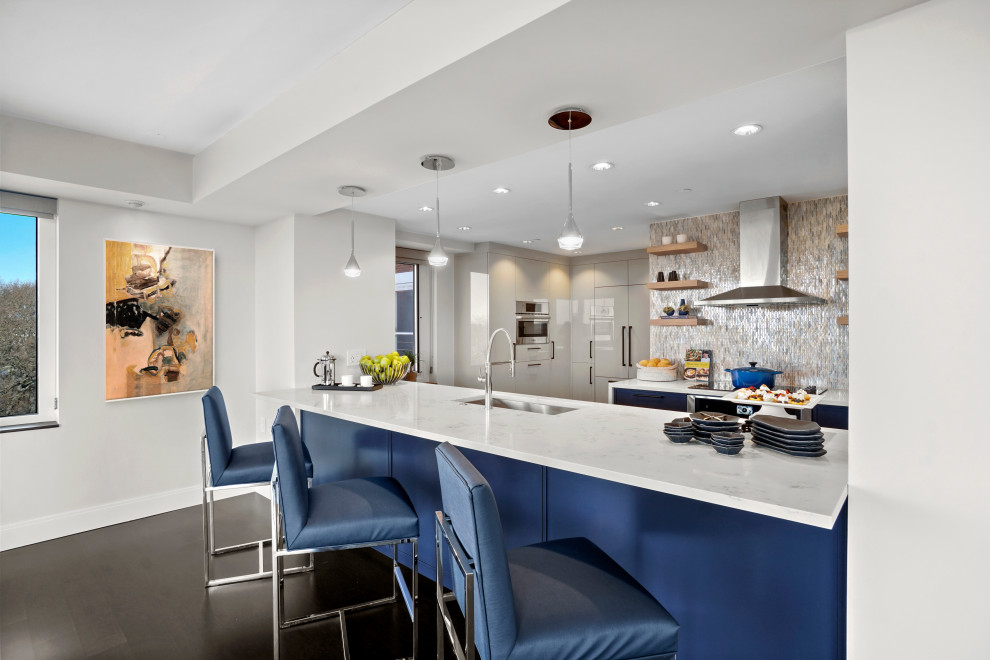 Design ideas for a mid-sized contemporary l-shaped eat-in kitchen in Boston with an undermount sink, shaker cabinets, blue cabinets, quartz benchtops, blue splashback, glass tile splashback, panelled appliances, dark hardwood floors, with island, brown floor and white benchtop.