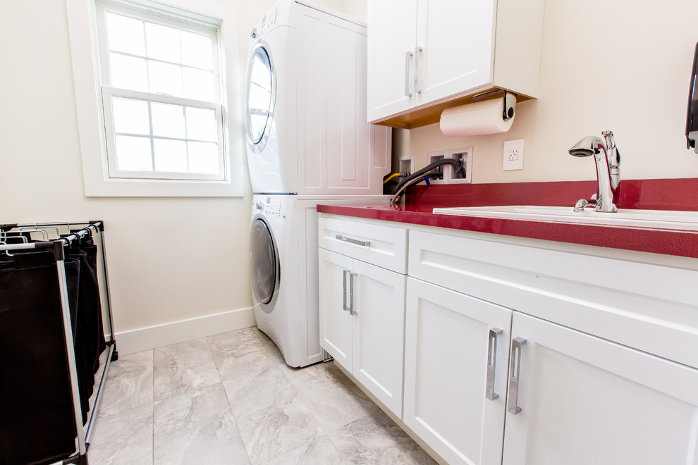 Inspiration for a small contemporary u-shaped dedicated laundry room in Other with a drop-in sink, recessed-panel cabinets, white cabinets, laminate benchtops, white walls, porcelain floors, a stacked washer and dryer, grey floor and red benchtop.