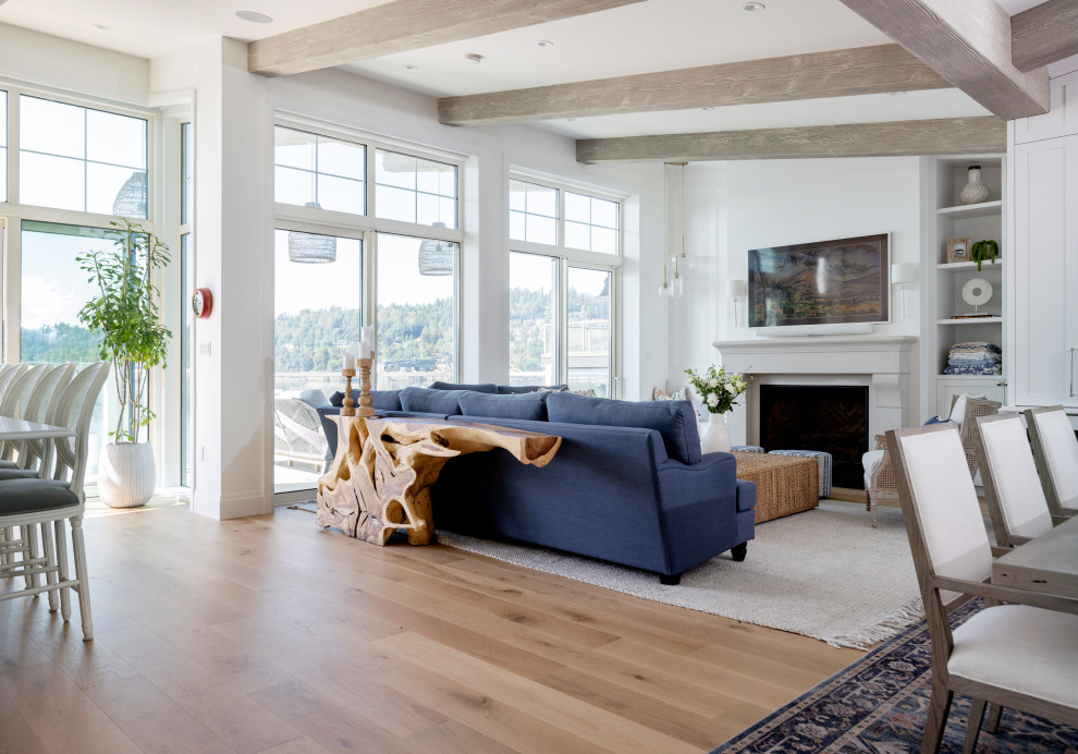 This is an example of a beach style open concept living room in Vancouver with white walls, light hardwood floors, a standard fireplace, a wall-mounted tv, beige floor, exposed beam and decorative wall panelling.