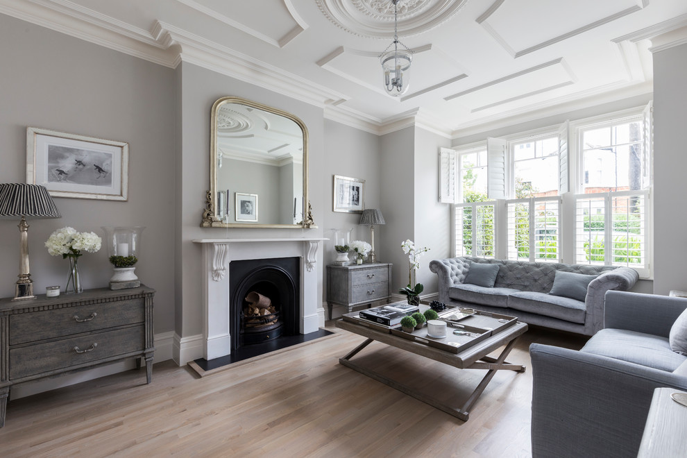 Design ideas for a large transitional enclosed living room in London with grey walls, light hardwood floors, a standard fireplace, a metal fireplace surround, no tv and brown floor.