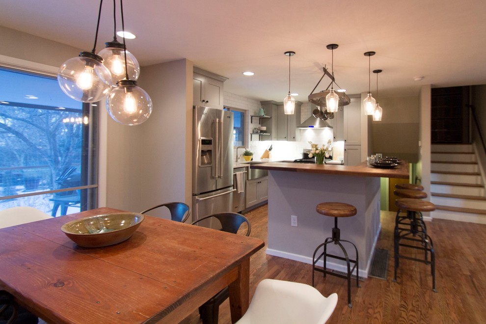 Mid-sized transitional l-shaped eat-in kitchen in Denver with a farmhouse sink, shaker cabinets, grey cabinets, quartz benchtops, white splashback, ceramic splashback, stainless steel appliances, medium hardwood floors and with island.