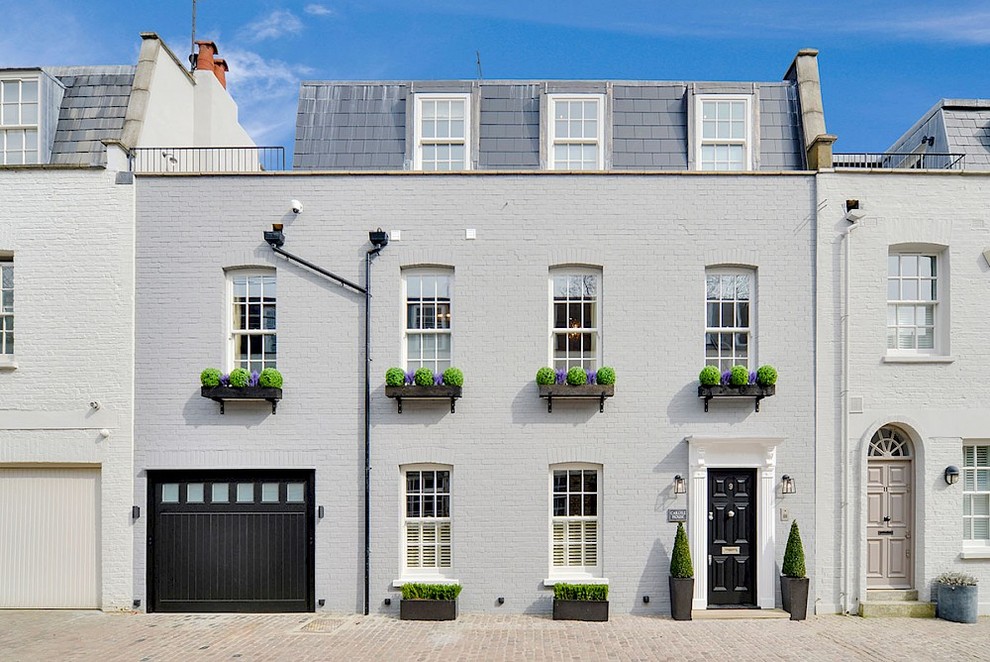 Photo of a mid-sized traditional three-storey grey townhouse exterior in London with a gambrel roof and a tile roof.