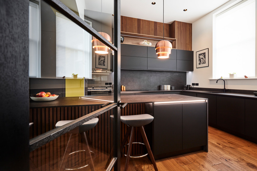 Immagine di una cucina minimal di medie dimensioni con ante lisce, ante nere, paraspruzzi nero, paraspruzzi con piastrelle in ceramica, elettrodomestici neri, pavimento in legno massello medio, pavimento marrone e top nero