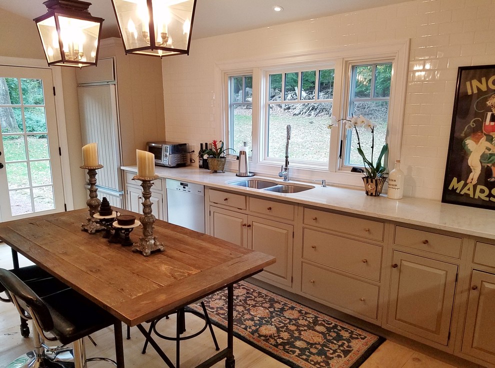 Photo of a small country l-shaped kitchen in Philadelphia with a double-bowl sink, recessed-panel cabinets, grey cabinets, quartz benchtops, white splashback, subway tile splashback, stainless steel appliances, light hardwood floors, no island and white benchtop.