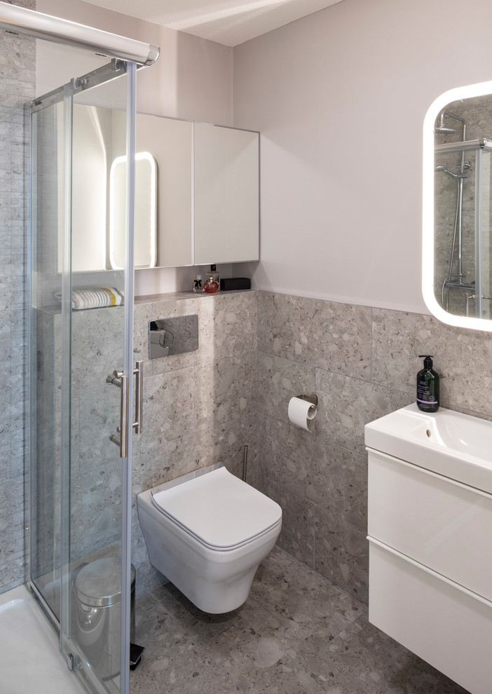 Small contemporary 3/4 bathroom in Dublin with flat-panel cabinets, white cabinets, a corner shower, a wall-mount toilet, gray tile, ceramic tile, grey walls, ceramic floors, a wall-mount sink, tile benchtops, grey floor, a sliding shower screen and grey benchtops.
