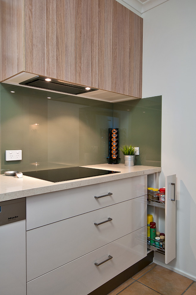 This is an example of a mid-sized modern l-shaped kitchen in Brisbane with a drop-in sink, flat-panel cabinets, beige cabinets, quartz benchtops, green splashback, glass sheet splashback, panelled appliances, ceramic floors and no island.