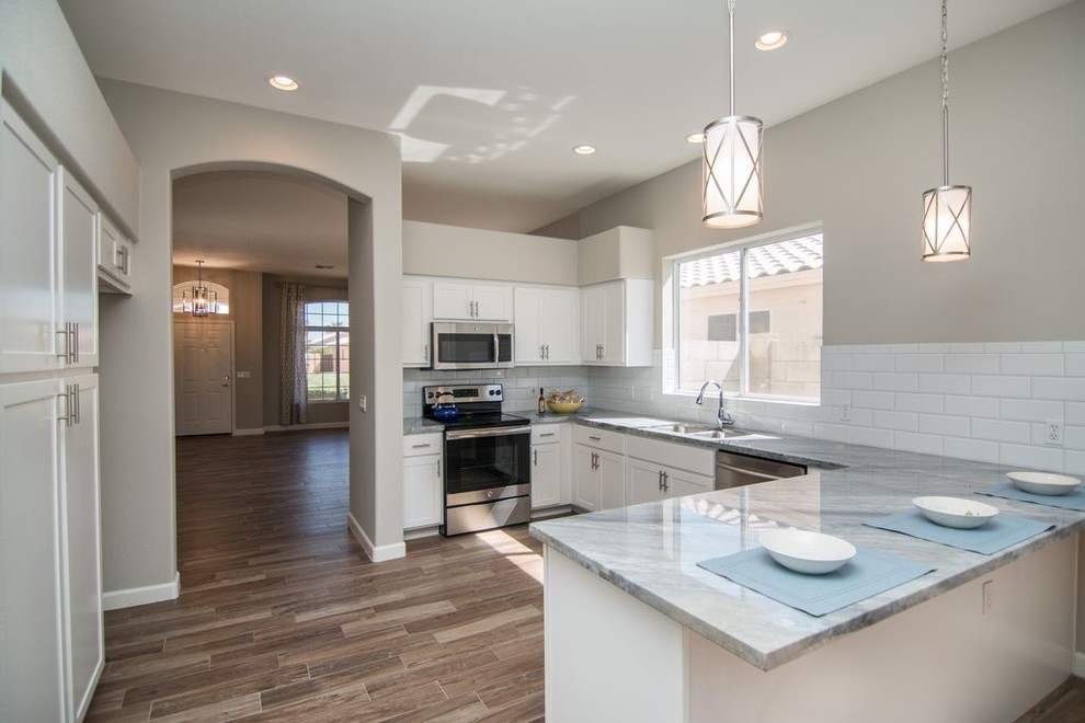 Mid-sized transitional u-shaped medium tone wood floor and brown floor kitchen photo in Phoenix with a double-bowl sink, shaker cabinets, white cabinets, quartzite countertops, white backsplash, subway tile backsplash, stainless steel appliances and a peninsula