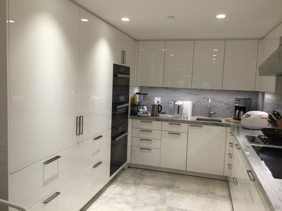 This is an example of a mid-sized modern u-shaped separate kitchen in New York with an undermount sink, flat-panel cabinets, white cabinets, multi-coloured splashback, marble splashback, black appliances, limestone floors, multi-coloured floor, quartzite benchtops and a peninsula.