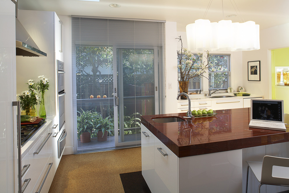 Photo of a mid-sized modern u-shaped eat-in kitchen in San Francisco with a drop-in sink, flat-panel cabinets, white cabinets, granite benchtops, red splashback, ceramic splashback, stainless steel appliances, cork floors, with island and orange floor.