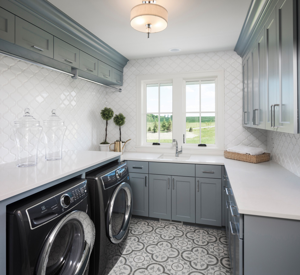 Klassische Waschküche in U-Form mit Schrankfronten im Shaker-Stil, grauen Schränken, Glas-Arbeitsplatte, Küchenrückwand in Weiß, Waschmaschine und Trockner nebeneinander, buntem Boden und weißer Arbeitsplatte in Minneapolis