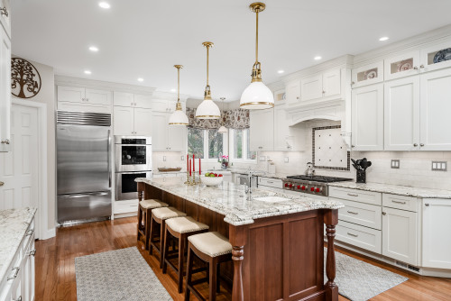 White shaker kitchen cabinet layout with granite countertops, a wooden island with stools, pendant lights, and stainless steel appliances.