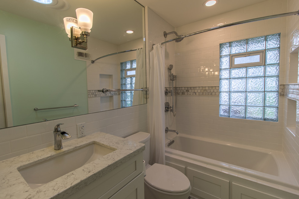 Photo of a mid-sized transitional master bathroom in Minneapolis with recessed-panel cabinets, white cabinets, an alcove tub, a shower/bathtub combo, a one-piece toilet, white tile, subway tile, blue walls, marble floors, an undermount sink, engineered quartz benchtops, white floor, a shower curtain and white benchtops.