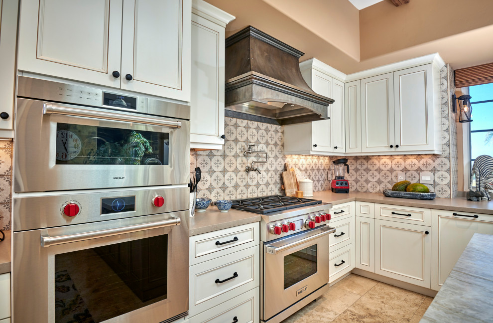 Open concept kitchen - mid-sized rustic galley travertine floor, beige floor and exposed beam open concept kitchen idea in Denver with a farmhouse sink, recessed-panel cabinets, white cabinets, quartz countertops, multicolored backsplash, stone tile backsplash, stainless steel appliances, an island and brown countertops