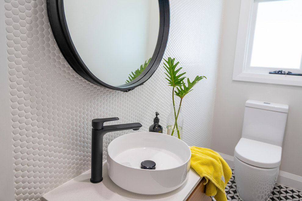 Mid-sized contemporary powder room in Brisbane with light wood cabinets, a one-piece toilet, white tile, mosaic tile, white walls, cement tiles, a vessel sink, engineered quartz benchtops, black floor and white benchtops.