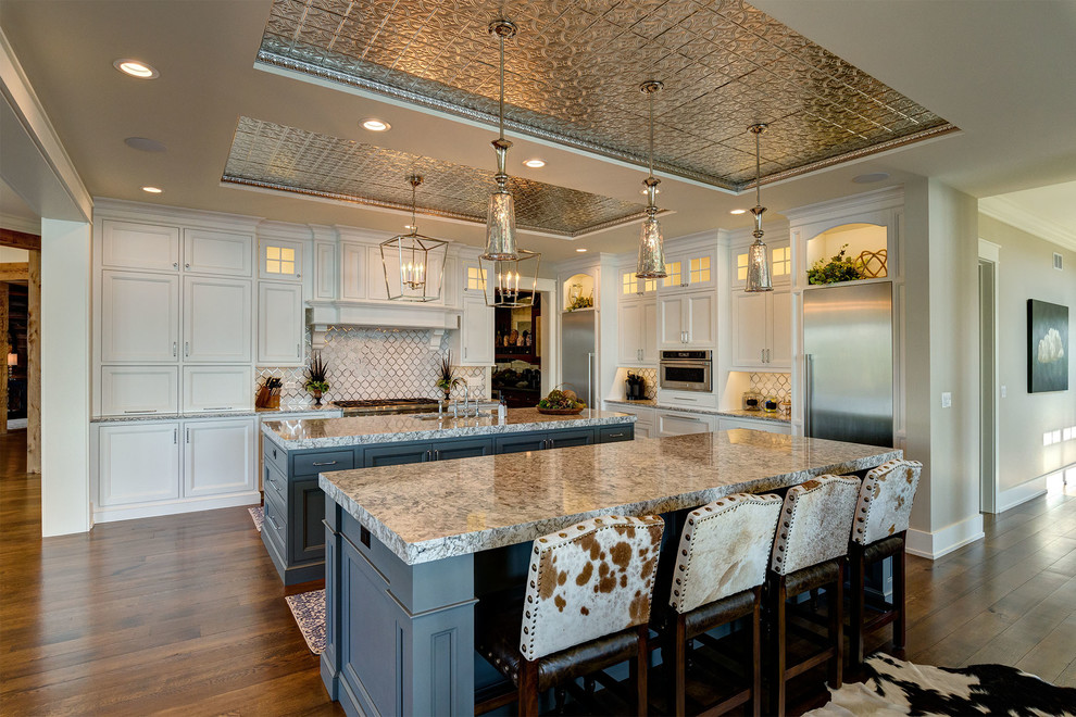 Inspiration for a l-shaped kitchen in Phoenix with an undermount sink, shaker cabinets, white cabinets, white splashback, stainless steel appliances, dark hardwood floors and multiple islands.