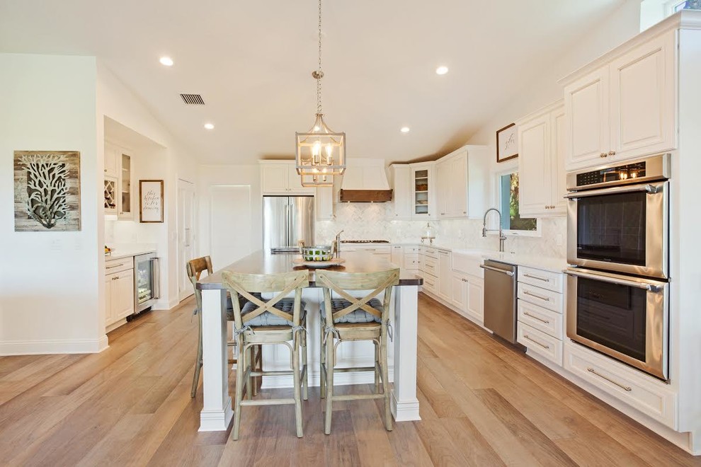 Country u-shaped eat-in kitchen in Jacksonville with a farmhouse sink, white cabinets, quartz benchtops, white splashback, glass tile splashback, stainless steel appliances, with island, white benchtop, raised-panel cabinets and medium hardwood floors.