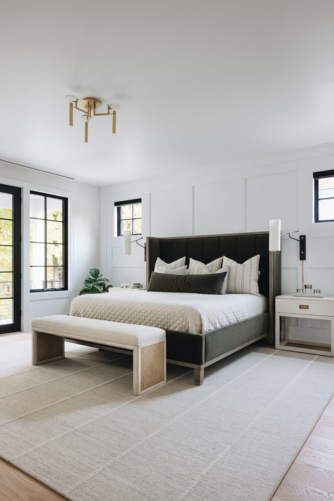 Primary Bedroom - Bedroom featuring white walls, wainscoting, reading lights, white nightstands, velvet bed, hardwood flooring, gold chandelier, and black windows.