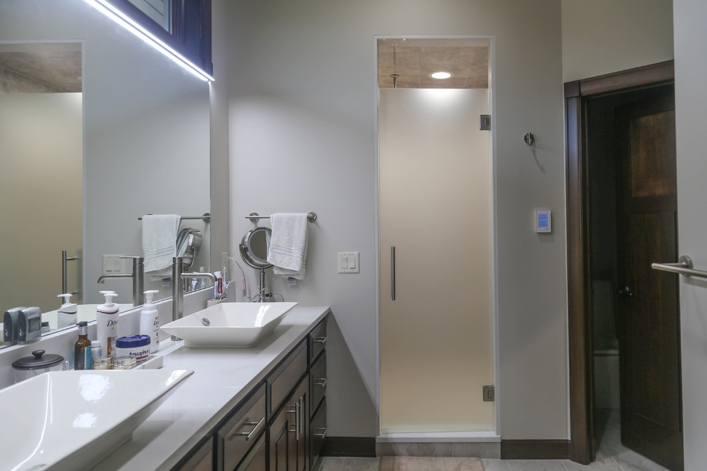 Example of a mid-sized transitional master beige tile and porcelain tile porcelain tile and beige floor alcove shower design with raised-panel cabinets, dark wood cabinets, a two-piece toilet, white walls, a vessel sink, quartzite countertops and a hinged shower door