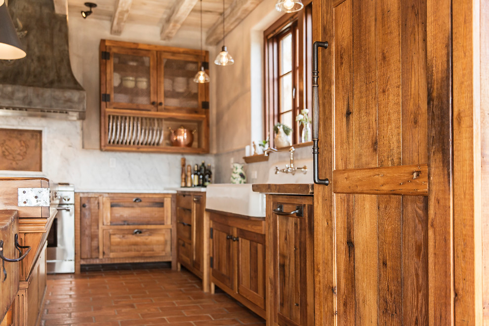 This is an example of a mid-sized country l-shaped eat-in kitchen in Nashville with a farmhouse sink, shaker cabinets, distressed cabinets, marble benchtops, white splashback, stone slab splashback, panelled appliances, terra-cotta floors, with island, red floor and white benchtop.