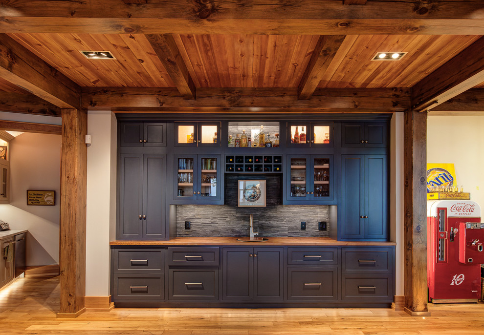 Inspiration for a transitional single-wall wet bar in Toronto with blue cabinets, grey splashback, medium hardwood floors, glass-front cabinets, wood benchtops and brown benchtop.