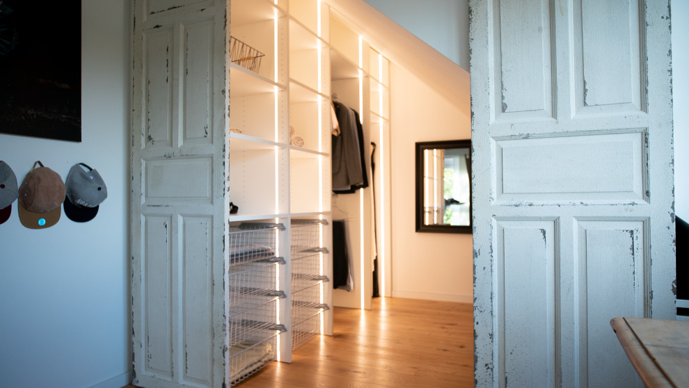 Medium sized scandi walk-in wardrobe in Munich with white cabinets, light hardwood flooring and brown floors.