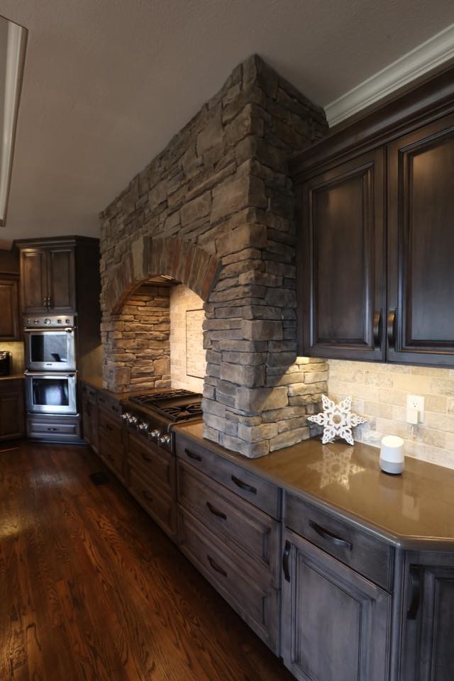 Large country u-shaped eat-in kitchen in Kansas City with a single-bowl sink, raised-panel cabinets, grey cabinets, granite benchtops, brown splashback, travertine splashback, stainless steel appliances, dark hardwood floors, with island, brown floor and brown benchtop.