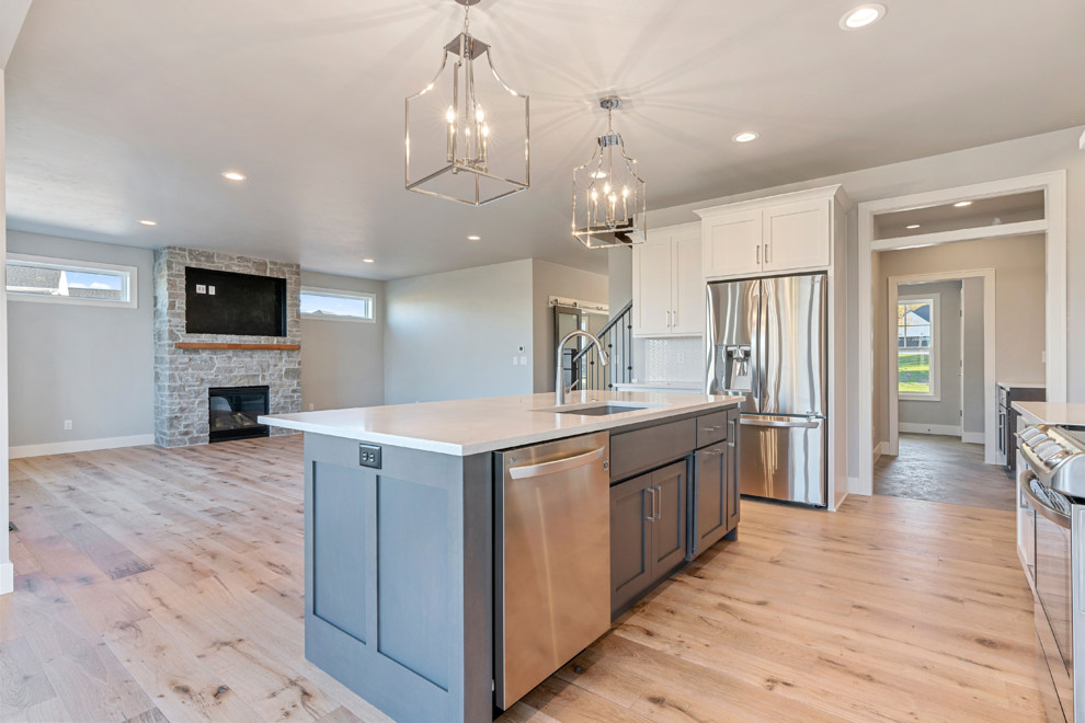 Transitional l-shaped light wood floor eat-in kitchen photo with an undermount sink, shaker cabinets, gray cabinets, quartz countertops, white backsplash, mosaic tile backsplash, stainless steel appliances, an island and white countertops