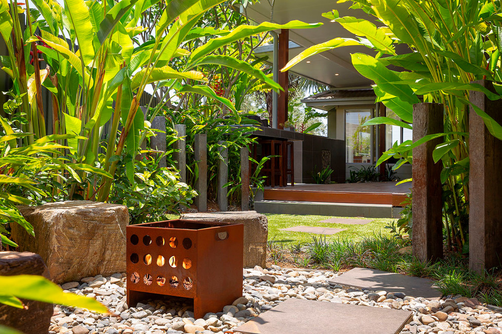 Immagine di un giardino tropicale esposto a mezz'ombra dietro casa con un focolare, pedane e recinzione in legno