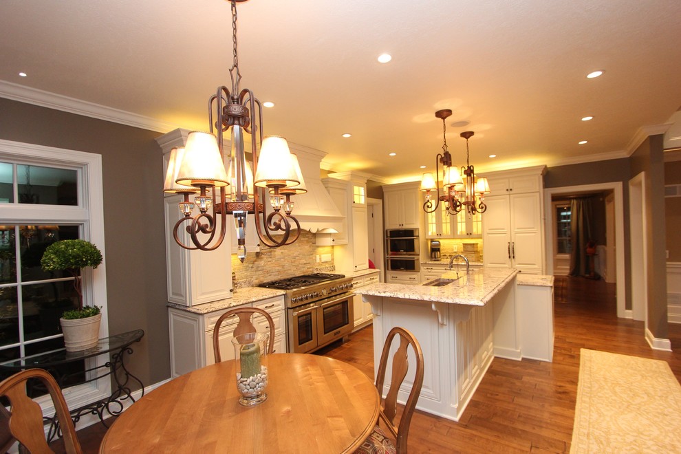 Inspiration for a large transitional l-shaped medium tone wood floor eat-in kitchen remodel with an undermount sink, raised-panel cabinets, white cabinets, granite countertops, beige backsplash, glass tile backsplash, stainless steel appliances, gray walls and an island