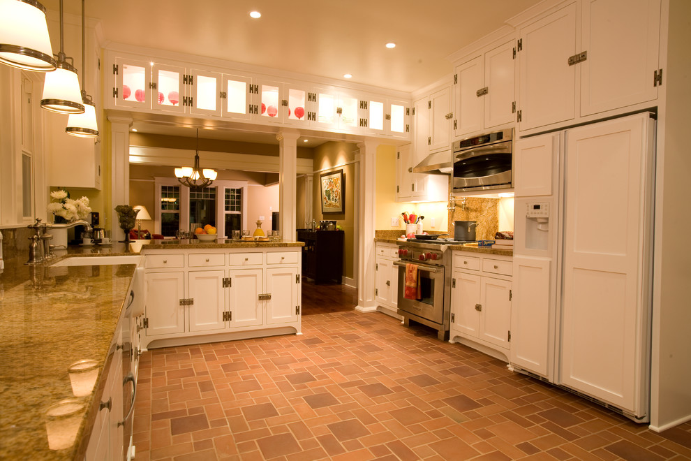 Photo of a mid-sized arts and crafts u-shaped eat-in kitchen in Charleston with beaded inset cabinets, white cabinets, granite benchtops, a farmhouse sink, stone slab splashback, stainless steel appliances and brick floors.