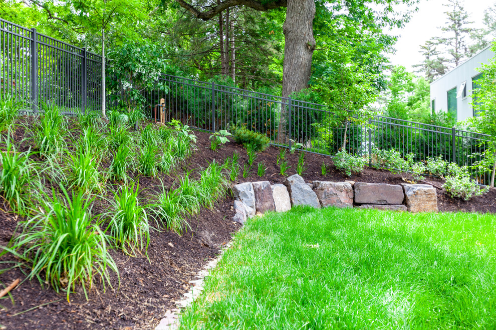 This is an example of a large modern sloped garden in Minneapolis with a retaining wall and concrete pavers.