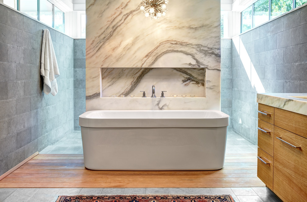 This is an example of a large modern master bathroom in Austin with an undermount sink, flat-panel cabinets, light wood cabinets, marble benchtops, a freestanding tub, an open shower, a one-piece toilet, gray tile, stone tile, white walls and limestone floors.