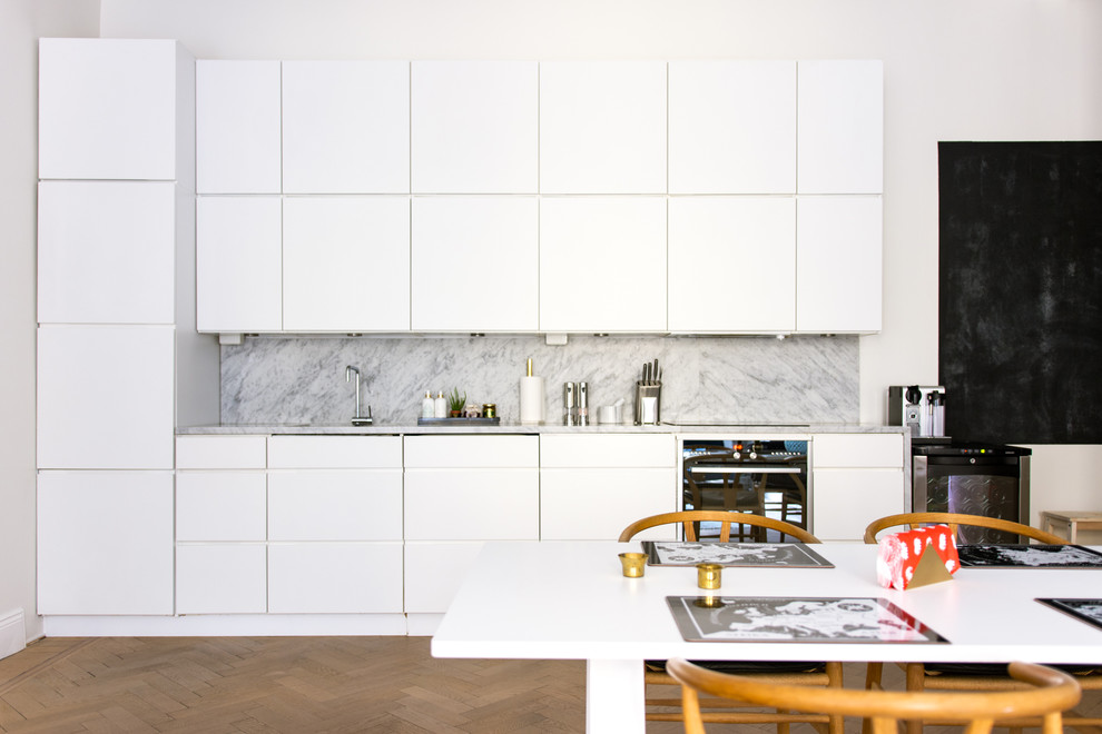 This is an example of a mid-sized scandinavian single-wall eat-in kitchen in Stockholm with flat-panel cabinets, white cabinets, marble benchtops, black appliances, medium hardwood floors and no island.