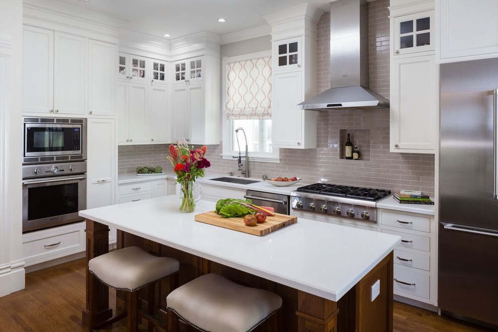 Design ideas for a large traditional l-shaped eat-in kitchen in San Francisco with an undermount sink, shaker cabinets, white cabinets, grey splashback, subway tile splashback, stainless steel appliances, dark hardwood floors, with island, brown floor, solid surface benchtops and white benchtop.