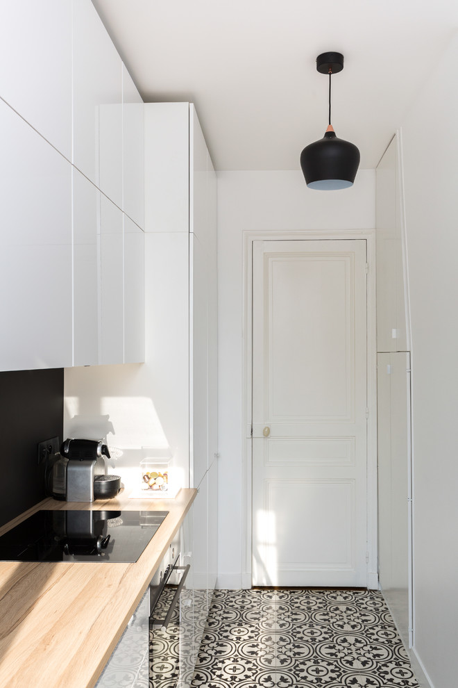 Design ideas for a mid-sized contemporary single-wall separate kitchen in Paris with wood benchtops, no island, a drop-in sink, flat-panel cabinets, white cabinets, black splashback, slate splashback, stainless steel appliances, cement tiles, multi-coloured floor and beige benchtop.